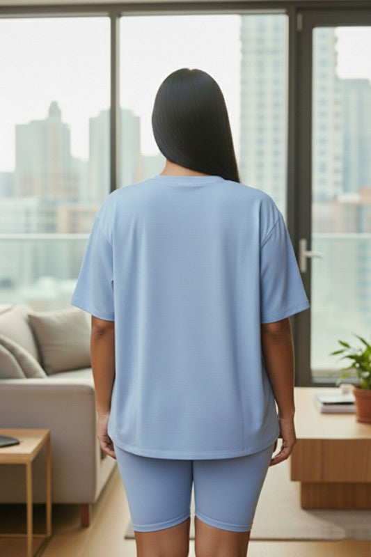 Person wearing a light blue outfit standing in a modern living room with large windows.