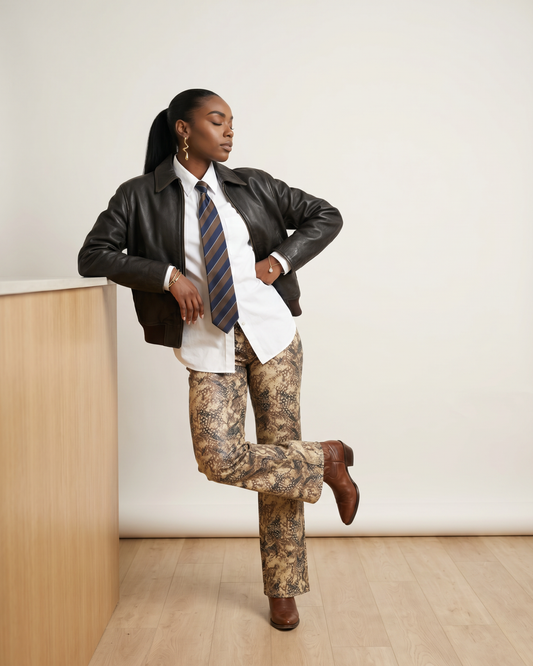 Female model wearing Bambi Cowgirl Wide Leg Jeans with a black leather jacket, white button-down shirt, striped tie, and brown boots.