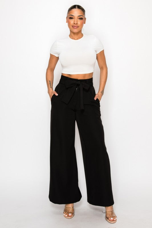 Woman wearing a white crop top and black wide-leg pants on a white background