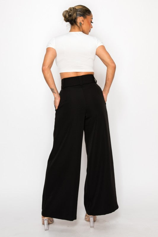 Woman wearing a white crop top and black wide-leg pants on a white background