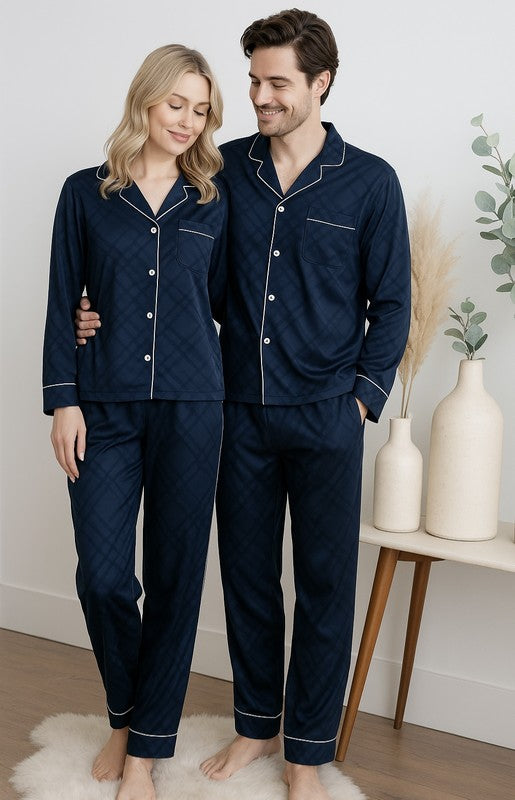 Man and woman wearing matching navy blue pajamas standing in a room with decorative elements.