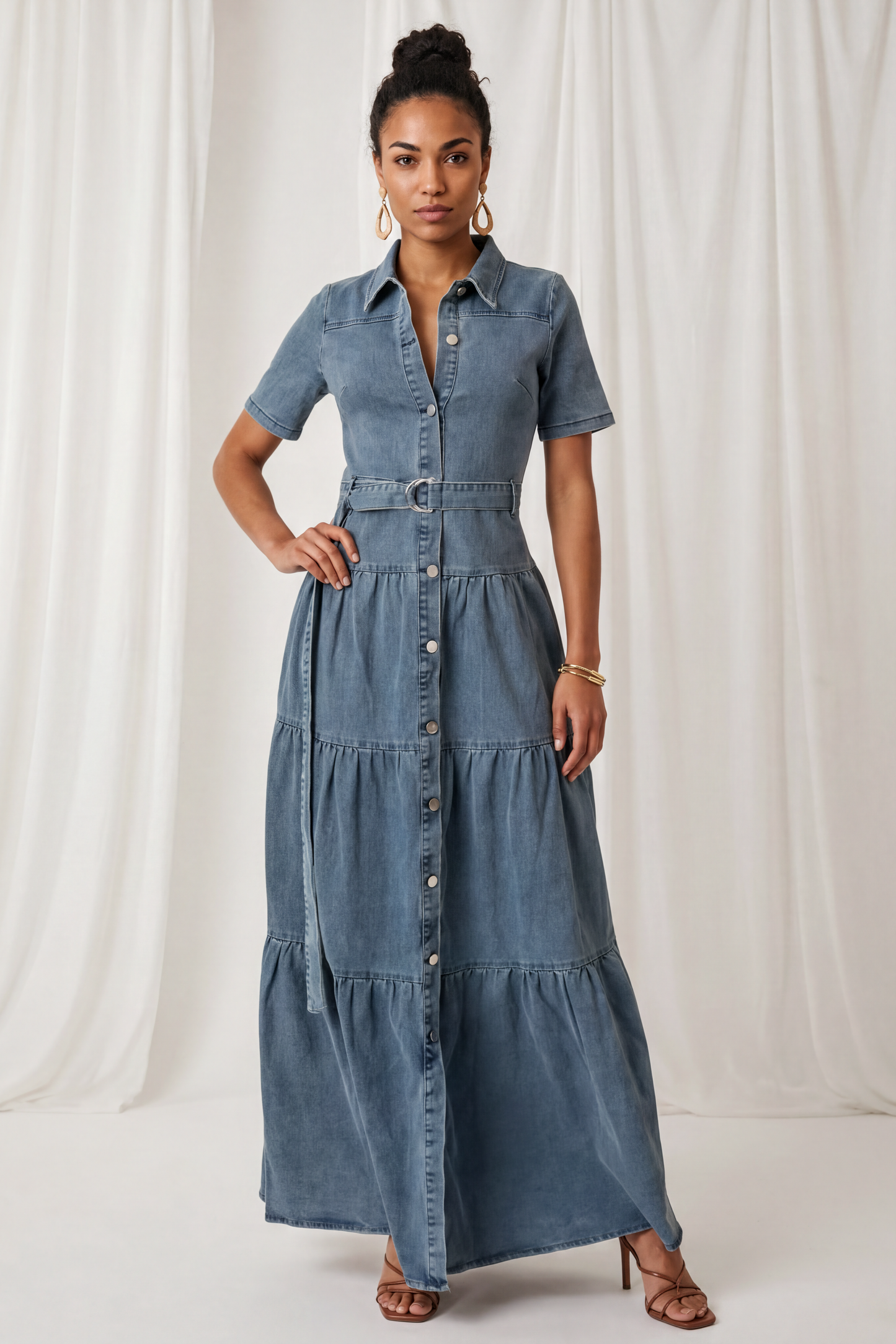 Front view of the Amora Denim Maxi Dress featuring short sleeves, a button-front closure, adjustable waist belt, and tiered maxi-length silhouette.